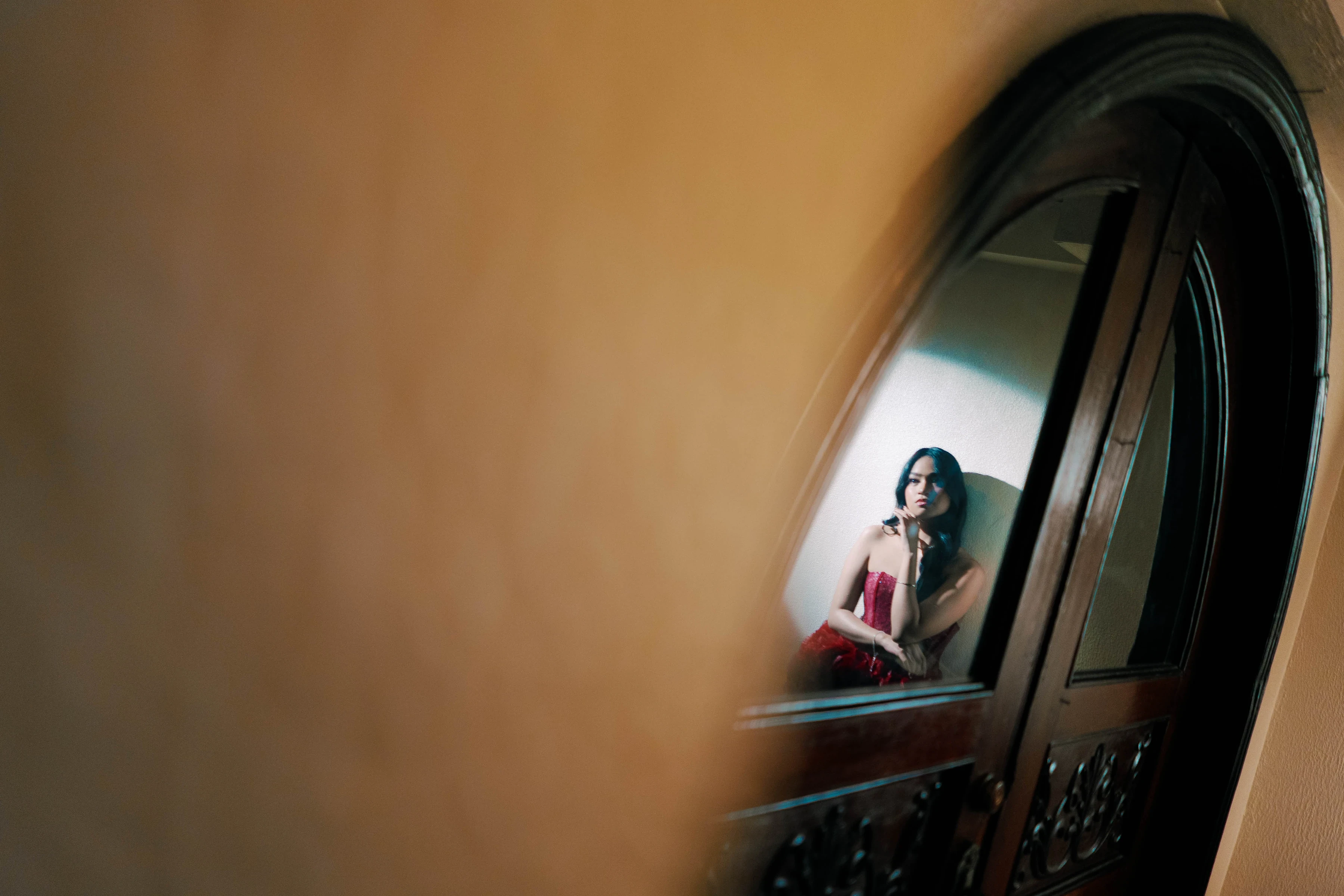Amber reflected in a dark arched mirror wearing a red gown