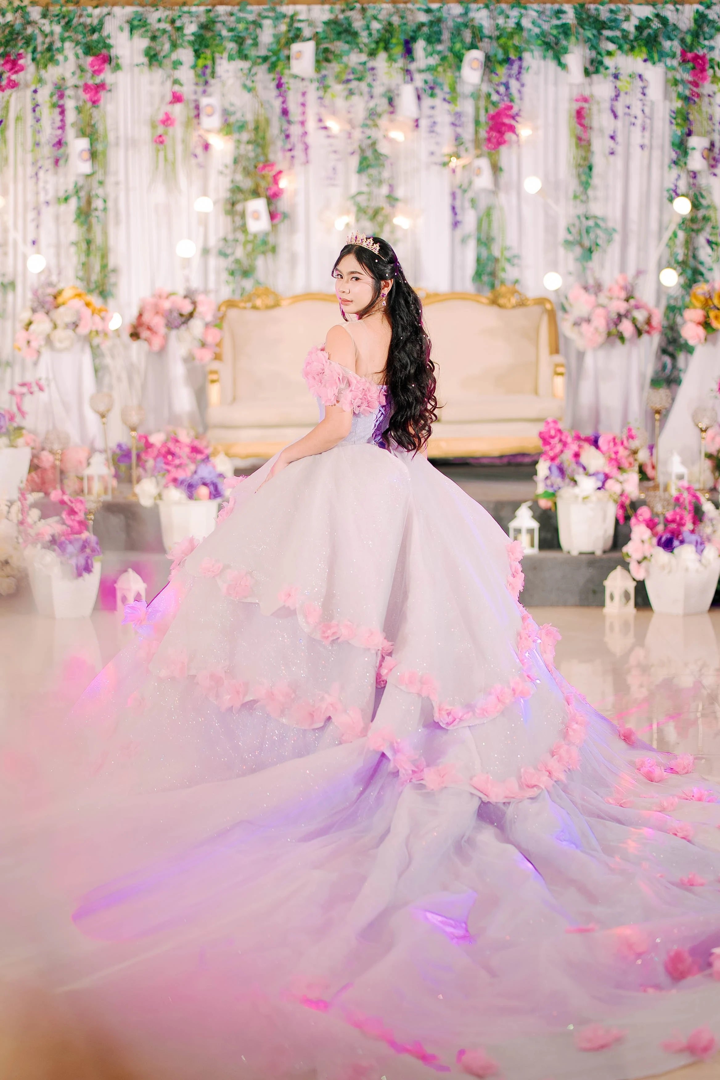 A woman in a pink gown sitting among pastel flowers