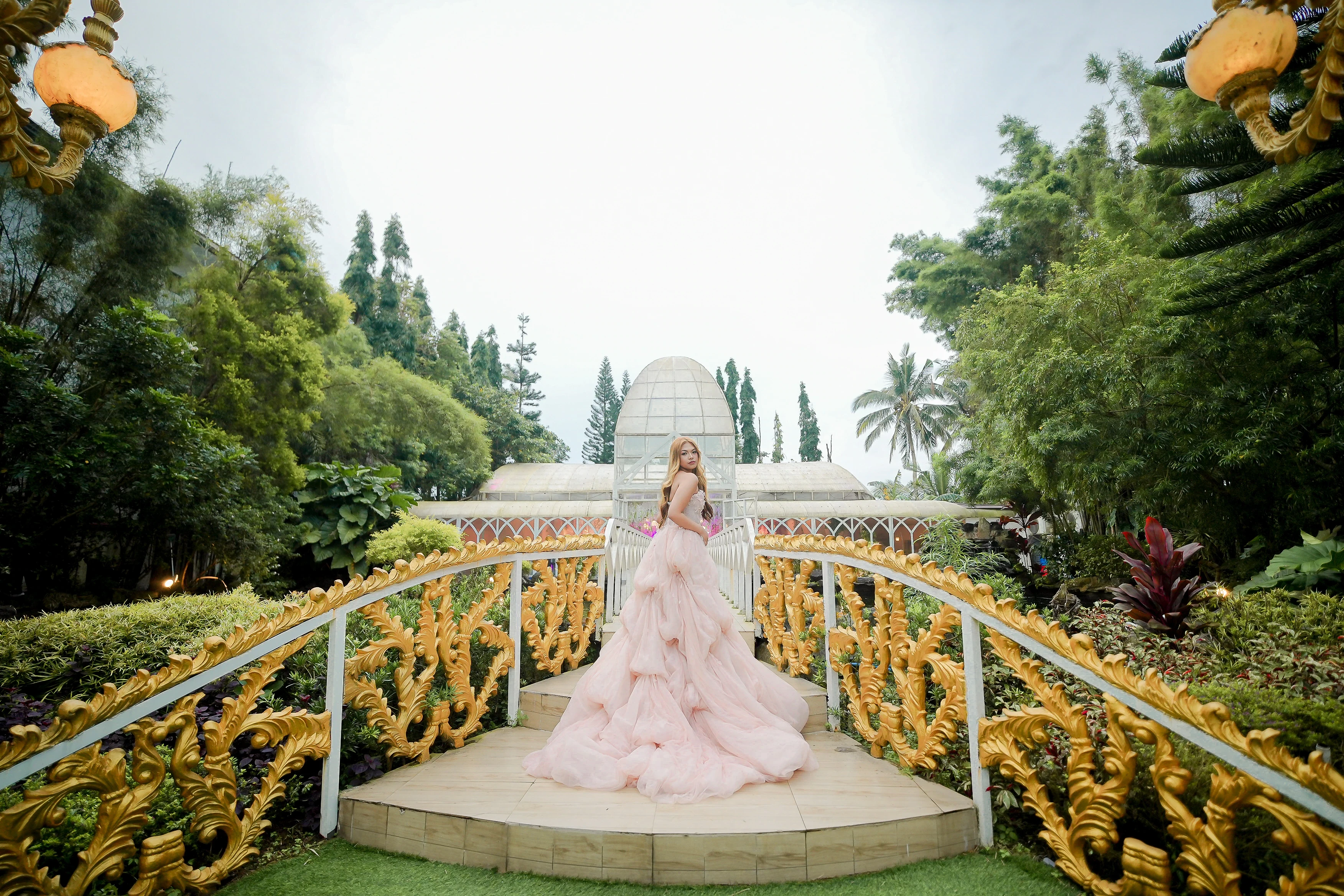A pink gown on an ornate bridge in a lush garden